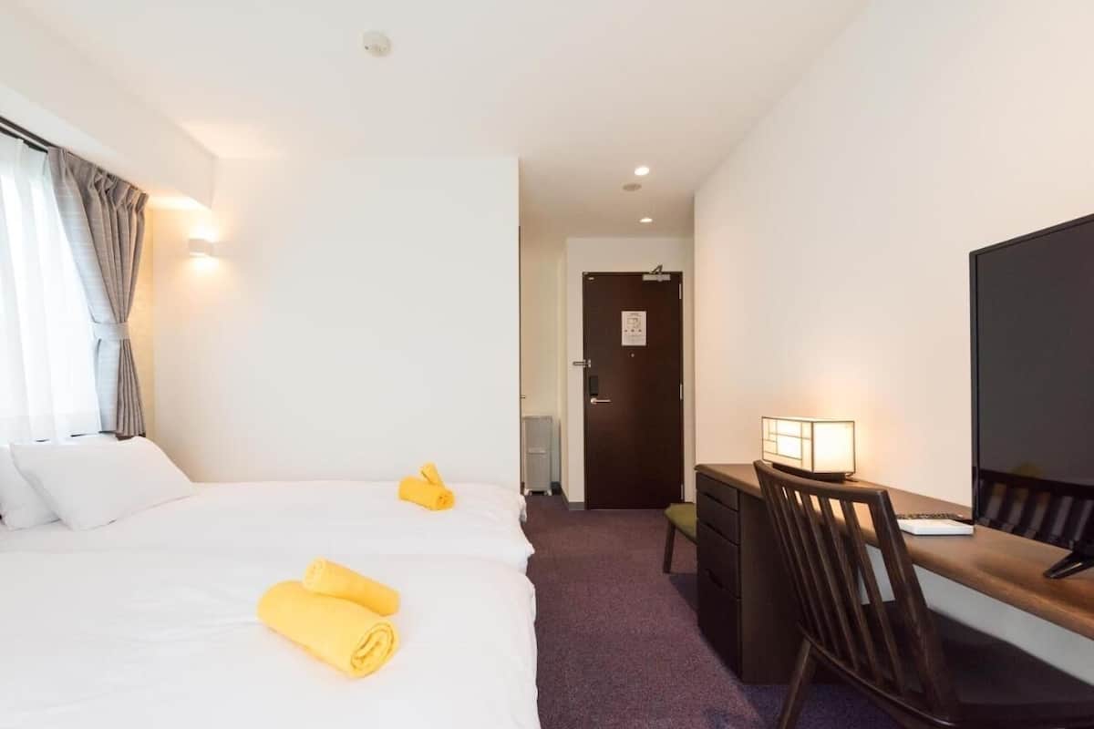 A hotel room with a bed, a desk with a chair, a TV, and a door.