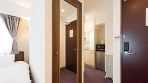 A hotel room with a bed, a wooden door, a kitchen area with a microwave, and a small refrigerator. - Serorin Light Hotel Tokyo (Tokyo)