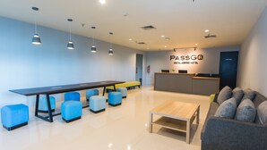 Un moderno vestíbulo de hotel con mostrador de recepción, una mesa larga con sillas azules, un sofá e iluminación colgante.
