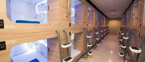 A row of private sleeping pods with individual beds, each pod has a number label, and there are steps leading to the beds.