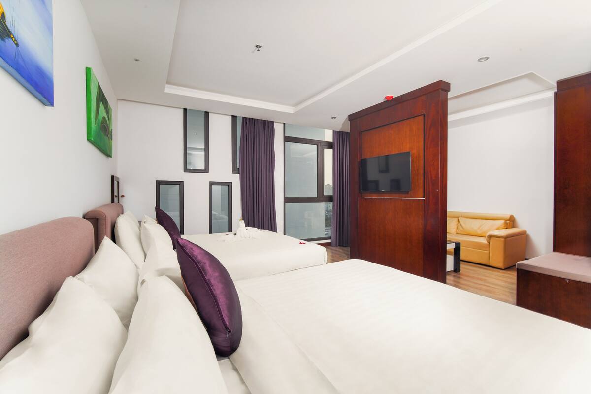 A hotel room with a large bed, a sofa, a TV, and a wooden wardrobe.
