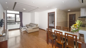 A modern living room with a sofa, a dining table with chairs, and a kitchen area visible through an open door. - Golden Sun Hotel (Da Nang)