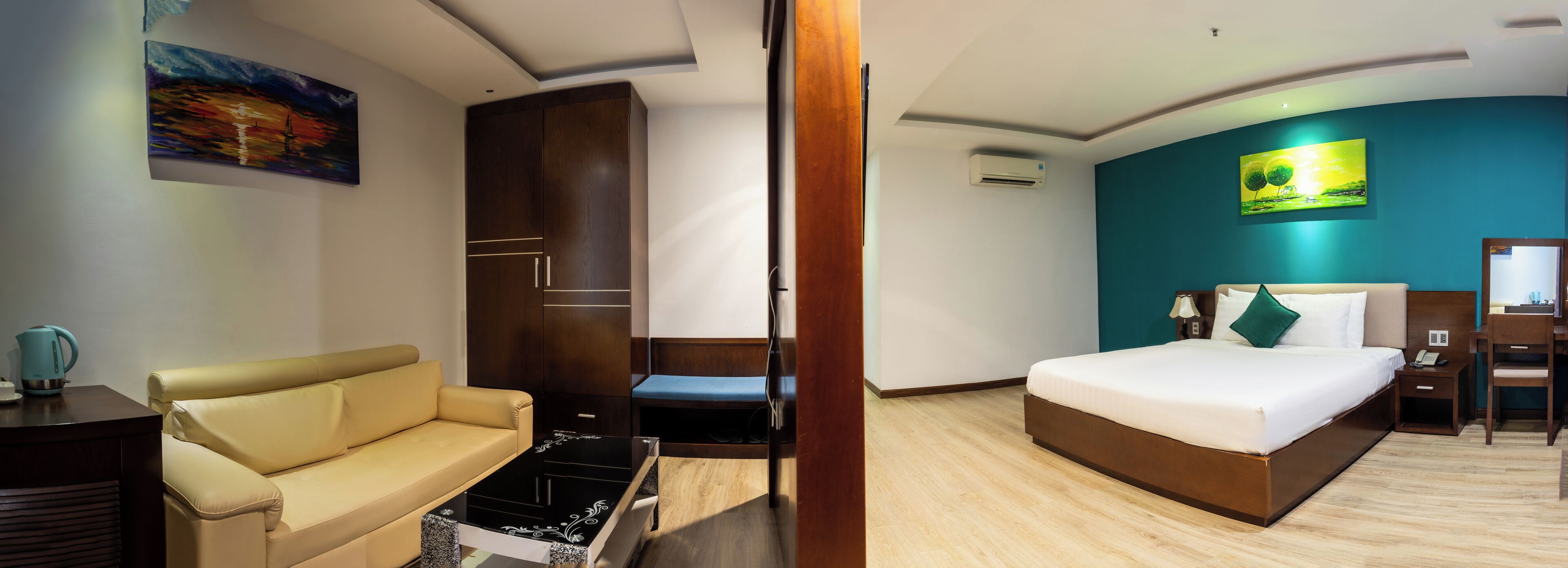 A hotel room with a bed, a sofa, a desk, and a painting on the wall.