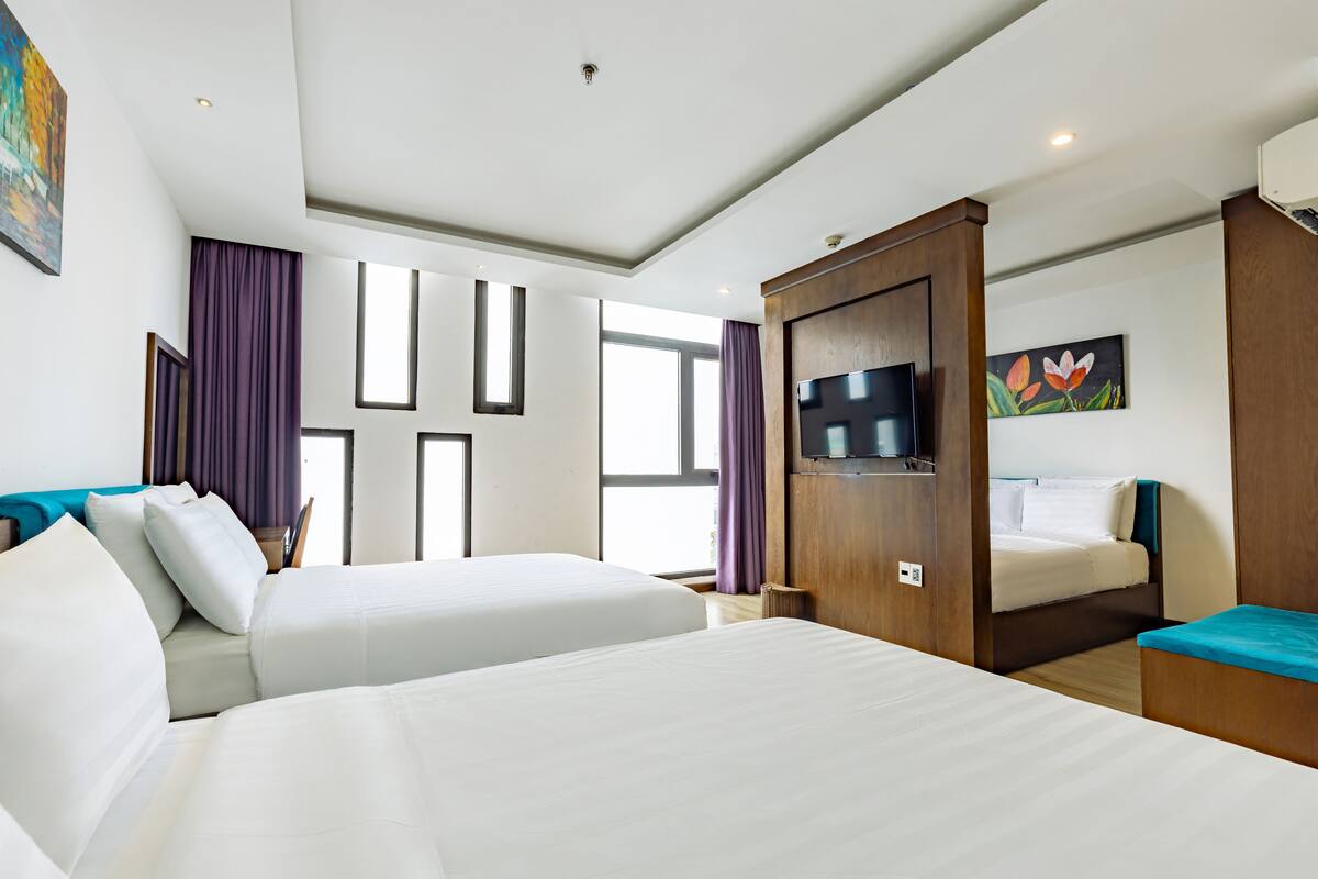 A hotel room with two beds, a TV, a painting, and a window with curtains.