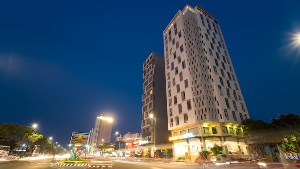 A multi-story hotel with illuminated signage, a roundabout, and a busy street with moving vehicles. - Golden Sun Hotel (Da Nang)
