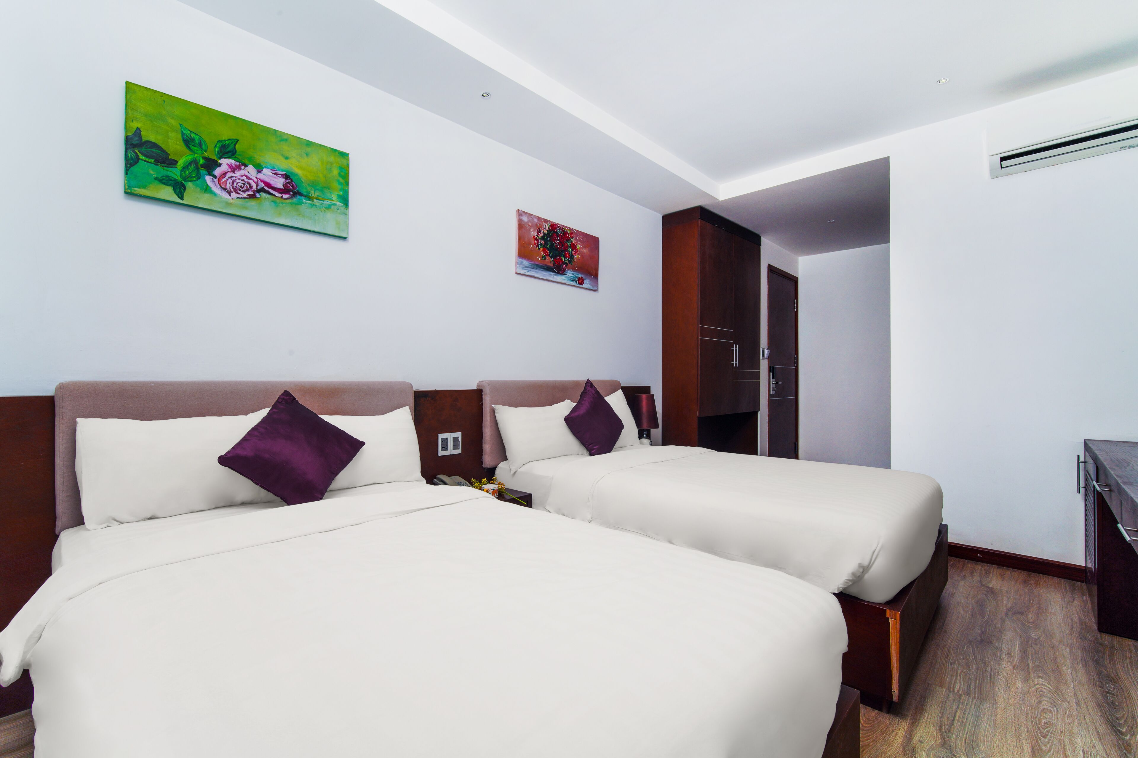 A hotel room with two beds, a wooden headboard, a painting on the wall, and a door leading to another room.