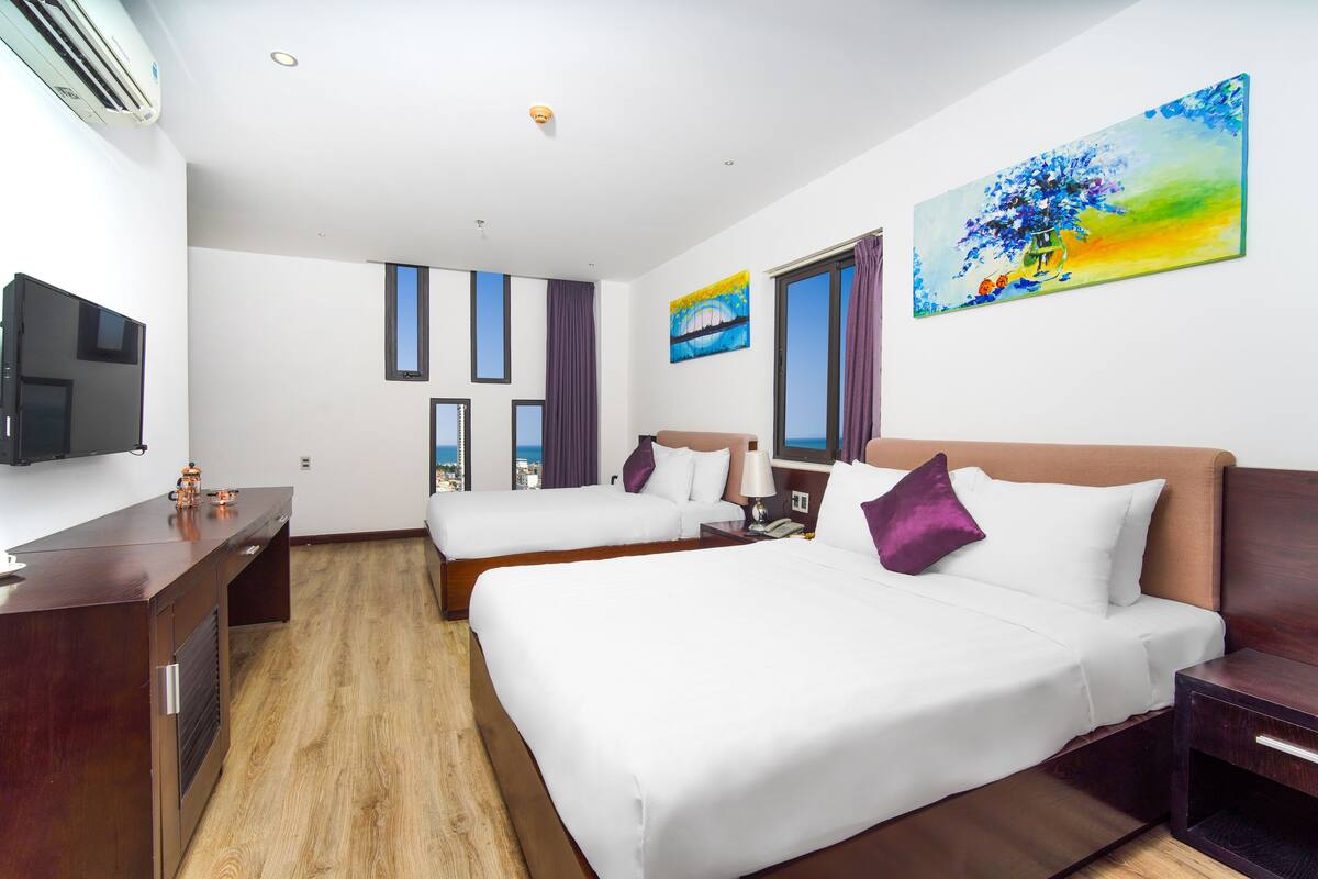 A hotel room with two beds, a TV, a desk, and artwork on the walls.