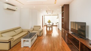A modern living room with a sofa, coffee table, TV stand, and wooden flooring. - Golden Sun Hotel (Da Nang)