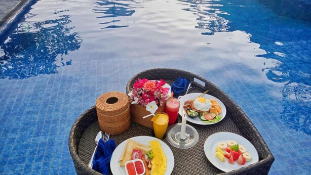 Un plateau en osier contenant des aliments pour le petit-déjeuner, placé près d’une piscine.