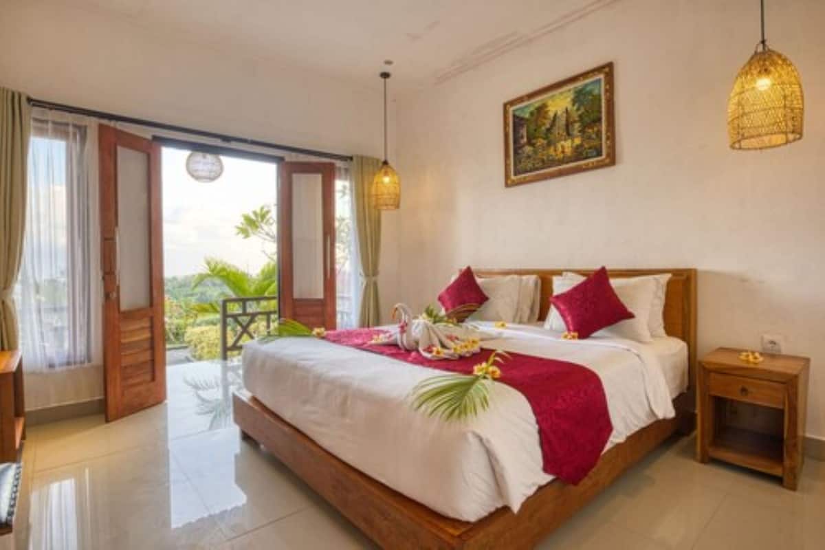 A spacious bedroom with a large bed, a wooden headboard, and a view of the outdoors through an open door.