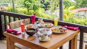 Une table en bois, dressée pour le petit-déjeuner, avec un saladier, une assiette d’œufs, des toasts et un verre de jus de fruits, le tout agrémenté d’une vue panoramique en arrière-plan.