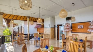 Un vaste espace dédié à la salle à manger, avec des tables et des chaises en bois, des lampes en osier suspendues et une vue sur l’espace extérieur.