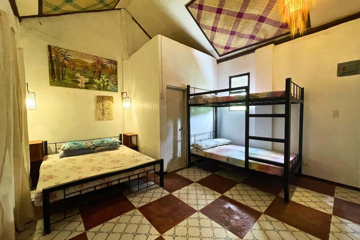 A dormitory room with a bunk bed, a single bed, and a checkered floor. There are wall decorations and a window.