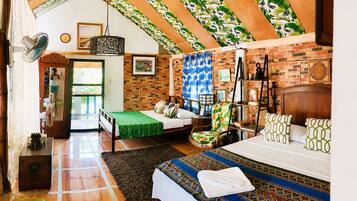 Un dormitorio con pared de ladrillo, cama de madera, colcha verde, alfombra estampada y ventilador de techo.