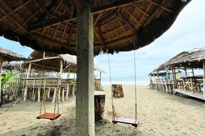 En strand med byggnader som har tak av halm och gungor av trä.