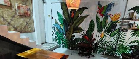 A room with a wooden table, a hanging light fixture, and a mural of tropical plants.