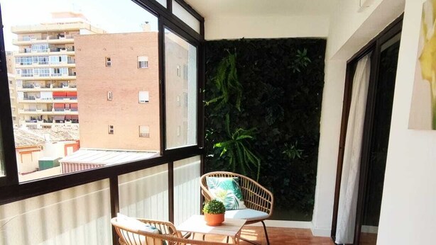 Un balcón con dos sillas de mimbre, una mesita y una planta en maceta.