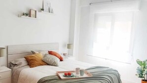 Un dormitorio con piso de madera, una cama con manta verde, una mesita de noche con lámpara y un ventilador de techo.
