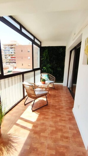 Un balcón con dos sillones de mimbre, una mesita y una planta en maceta.