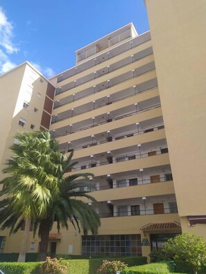 Un immeuble à plusieurs étages doté de balcons, d’un palmier et d’une enseigne indiquant le nom du bâtiment.