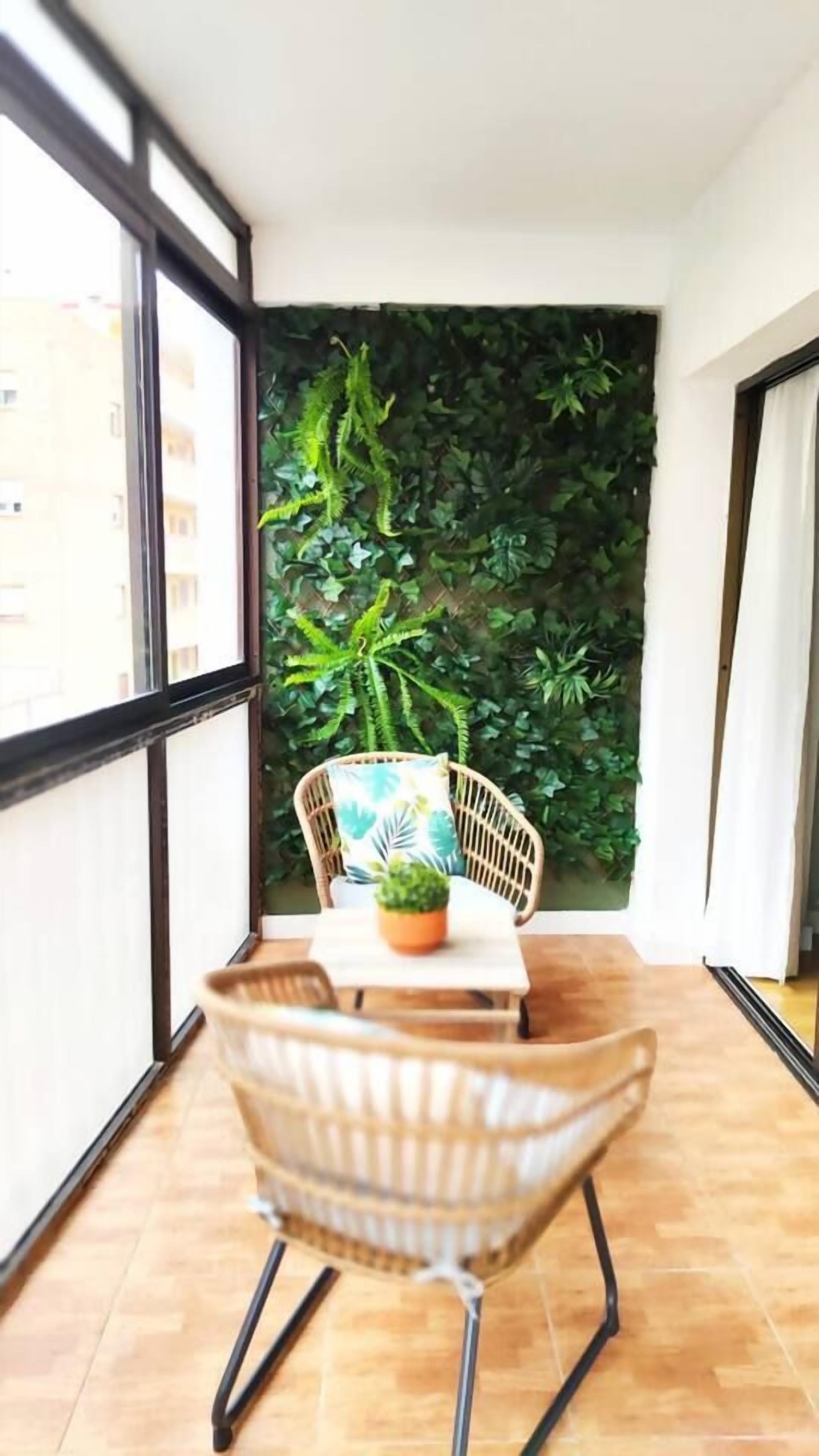 A balcony with a table, chairs, a potted plant, and a wall covered in green foliage.