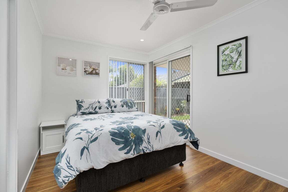 A bedroom with a bed, a ceiling fan, a window with a view, and a framed picture on the wall.