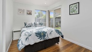 A bedroom with a bed, a ceiling fan, a window with a view, and a framed picture on the wall.