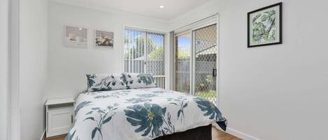 A bedroom with a bed, a ceiling fan, a window with a view, and a framed picture on the wall.