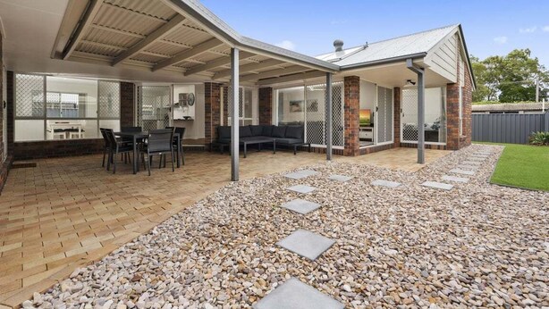 A covered outdoor patio with a brick floor, stone stepping stones, and a seating area with a table and chairs.