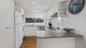 A modern kitchen with white cabinetry, a granite countertop, a clock, and a window with a view.