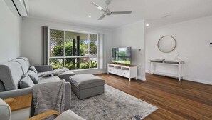 A living room with a sofa, ottoman, TV, white console, and a ceiling fan.