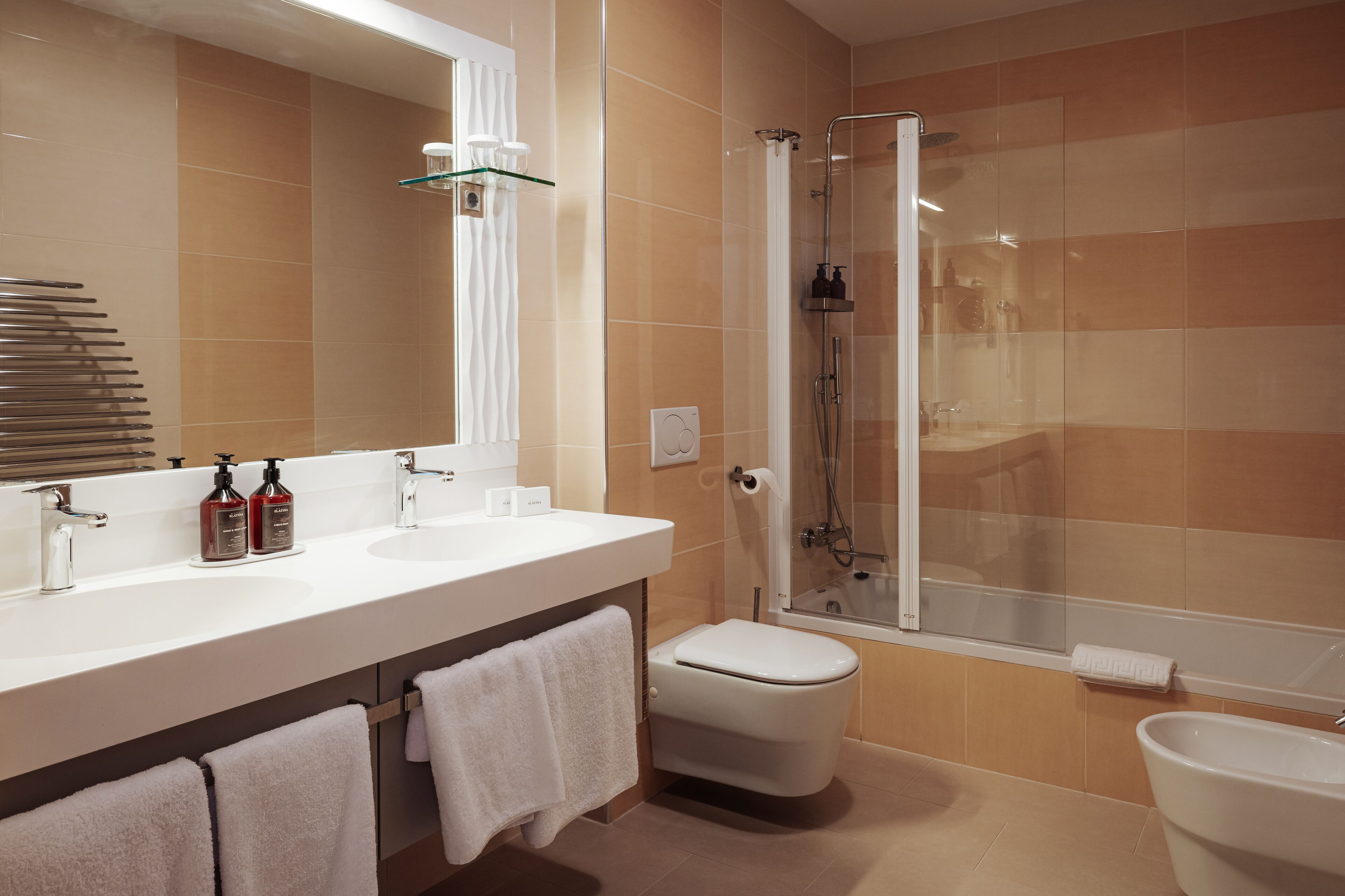 A modern bathroom with a glass-enclosed shower, a white sink with two bottles of soap, and a toilet.