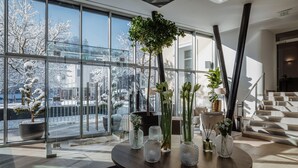 A modern interior with large windows, a round table with vases, and a staircase. - Hotel Slatina (Rogaska Slatina)