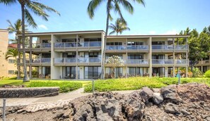 A multi-story hotel with balconies, a landscaped garden, and a rocky foreground. - Aloha Condos, Keauhou Kona Surf and Racquet Club, Condo 2-302, Oceanfront, AC (Kailua Kona)
