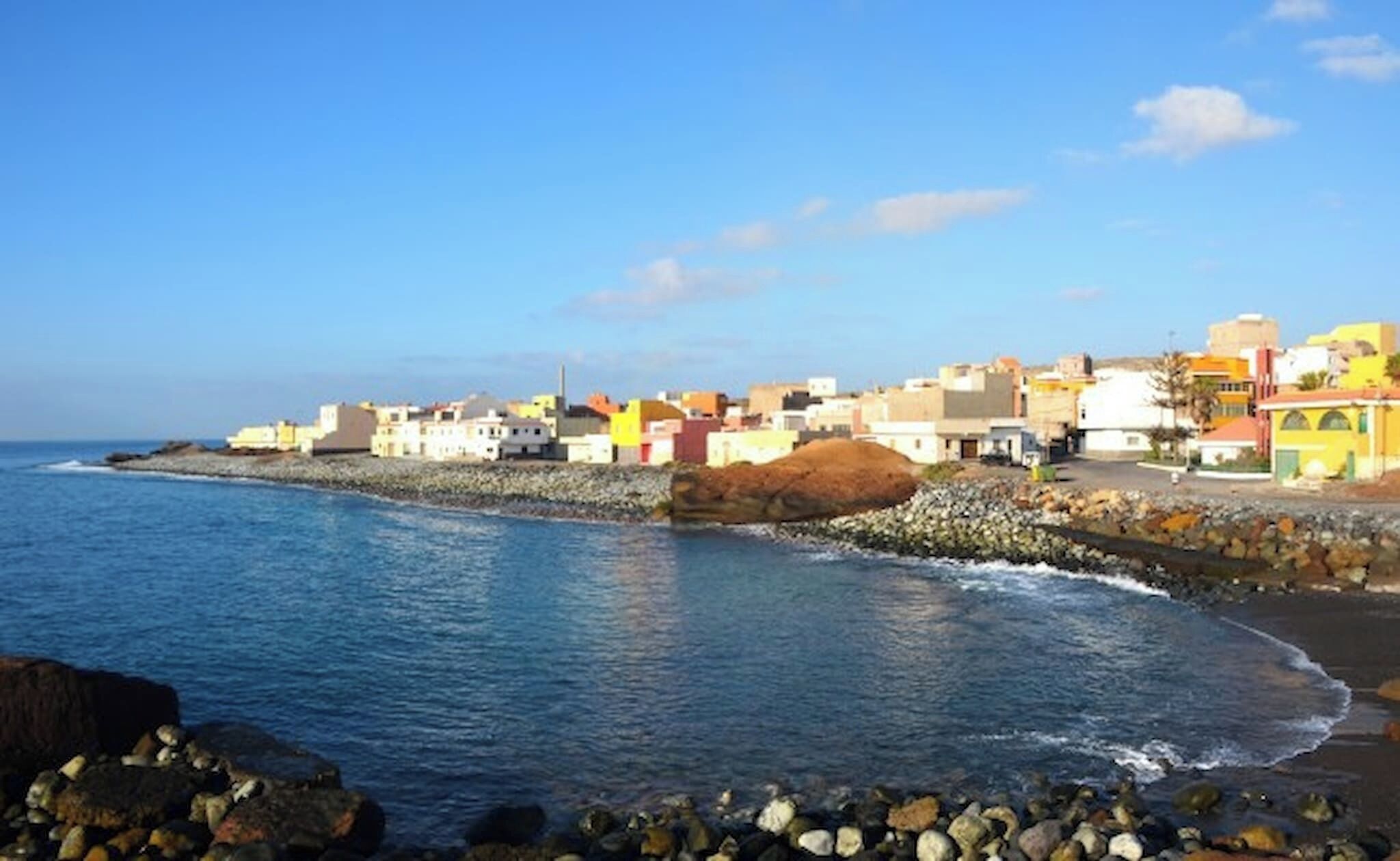 A coastal town with buildings along the shore, a rocky beach, and calm sea.