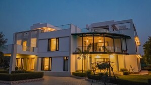 Una casa moderna de dos pisos con un balcón, ventanas amplias y una entrada bien iluminada.