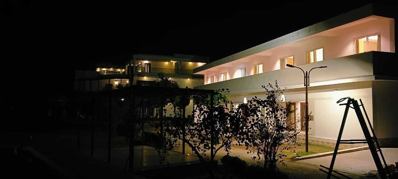 A modern hotel with multiple floors, illuminated windows, and a well-lit entrance area with trees and a street lamp.