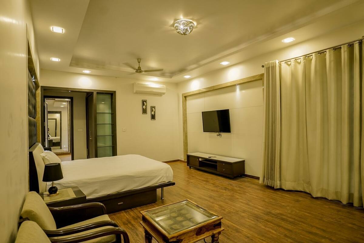 Habitación de hotel con cama, televisor, escritorio, silla, ventilador de techo y ventana con cortinas.