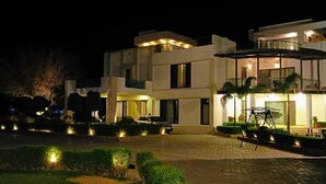 Una casa moderna de dos pisos con entrada pavimentada, mobiliario exterior e iluminacion visible desde afuera.