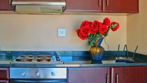 Une cuisine avec des armoires en bois, une hotte de cuisinière en acier inoxydable, une cuisinière et un vase rempli de roses rouges posé sur le comptoir.