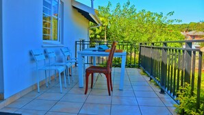 Une terrasse extérieure avec une table et des chaises, un fauteuil en osier et une rambarde.