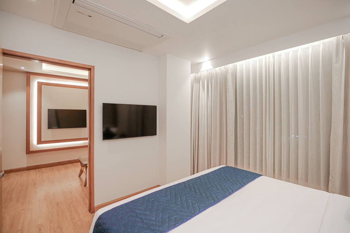 A modern hotel room with a large bed, a flat-screen TV mounted on the wall, and a large window with curtains.