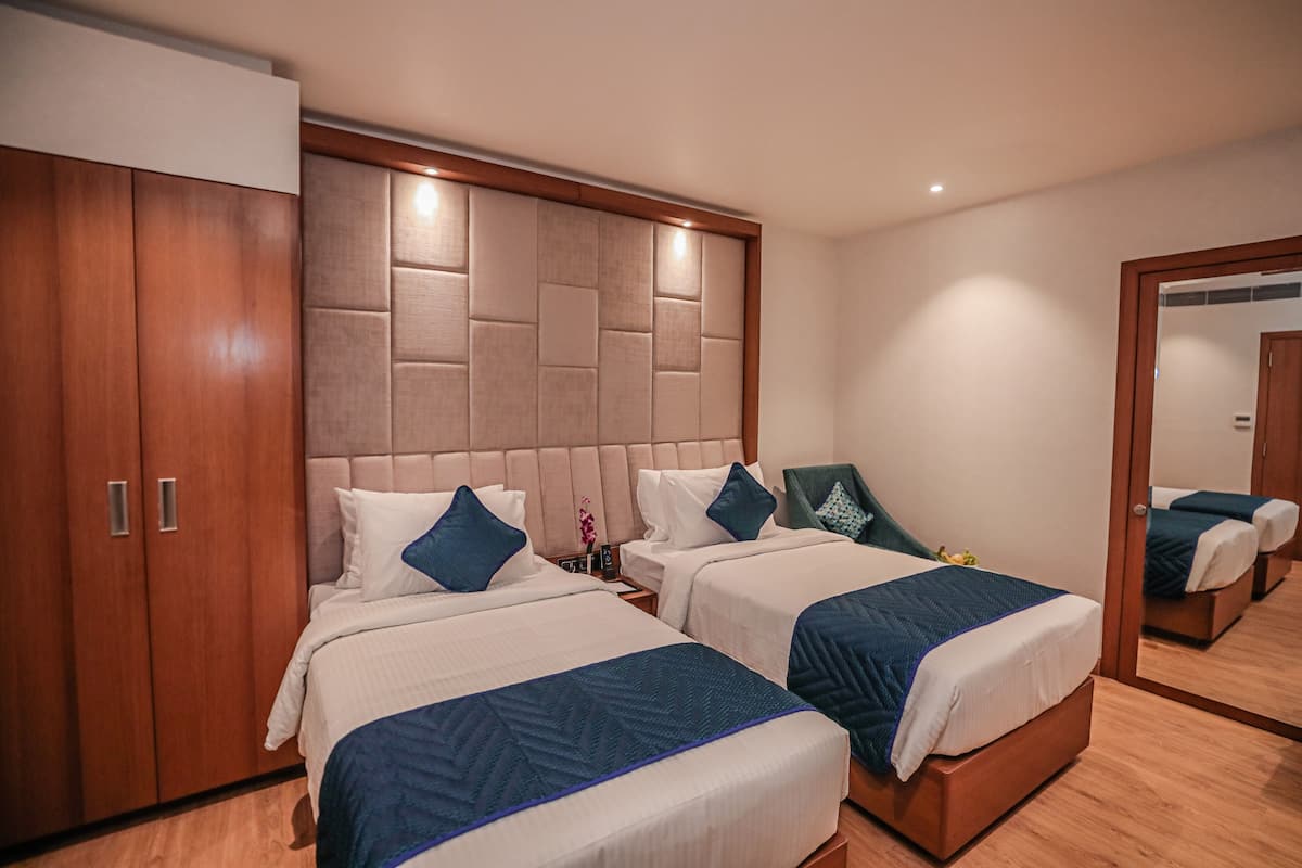 A hotel room with two beds, wooden wardrobe, and a large mirror.