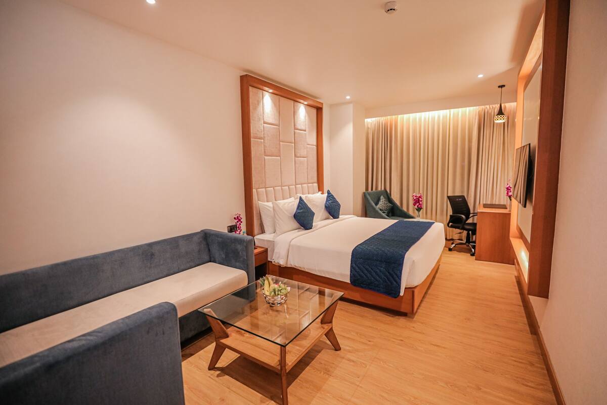 A hotel room with a bed, a sofa, a glass coffee table, a desk, and a chair.