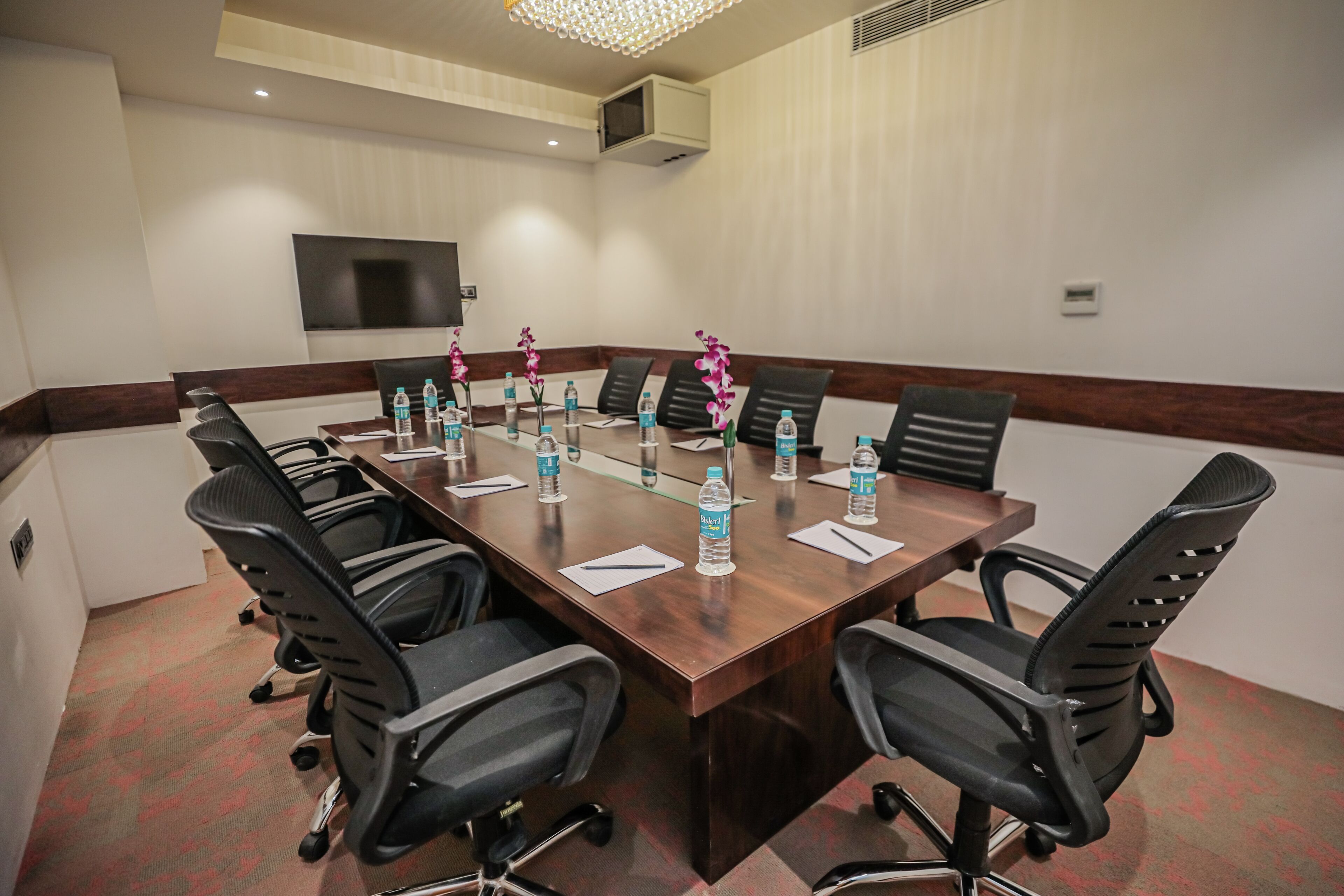 A conference room with a long table, black office chairs, water bottles, and a flat-screen TV on the wall.