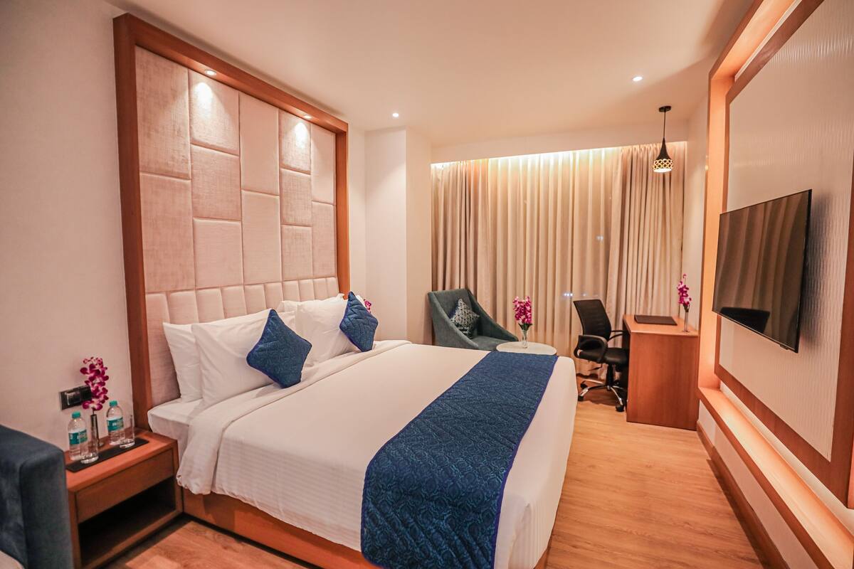 A hotel room with a large bed, a desk, a chair, a TV, and a curtain.