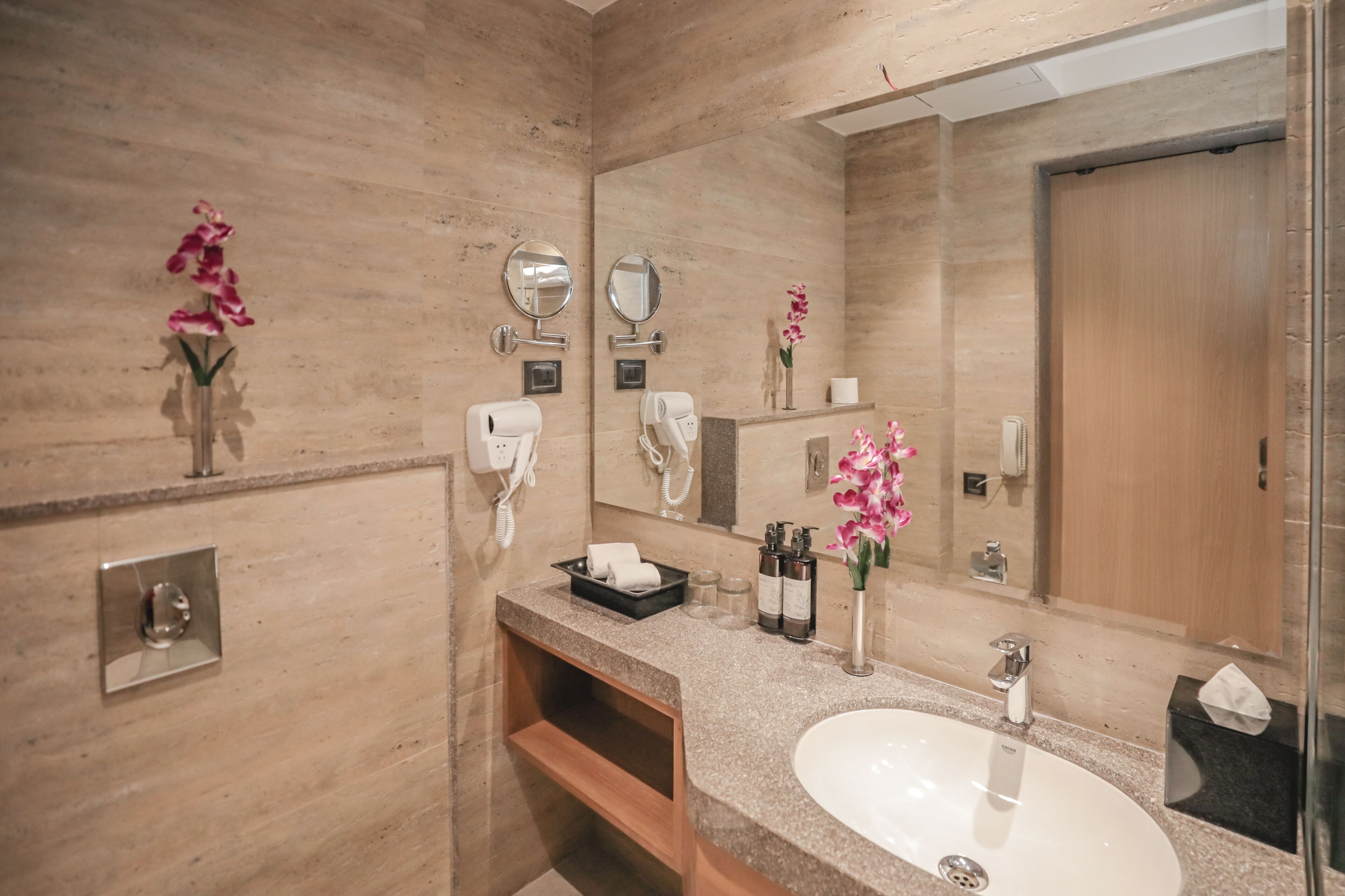 A modern bathroom with a large mirror, two hair dryers, a sink, and a vanity.