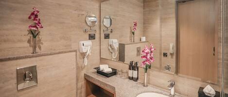 A modern bathroom with a large mirror, two hair dryers, a sink, and a vanity.