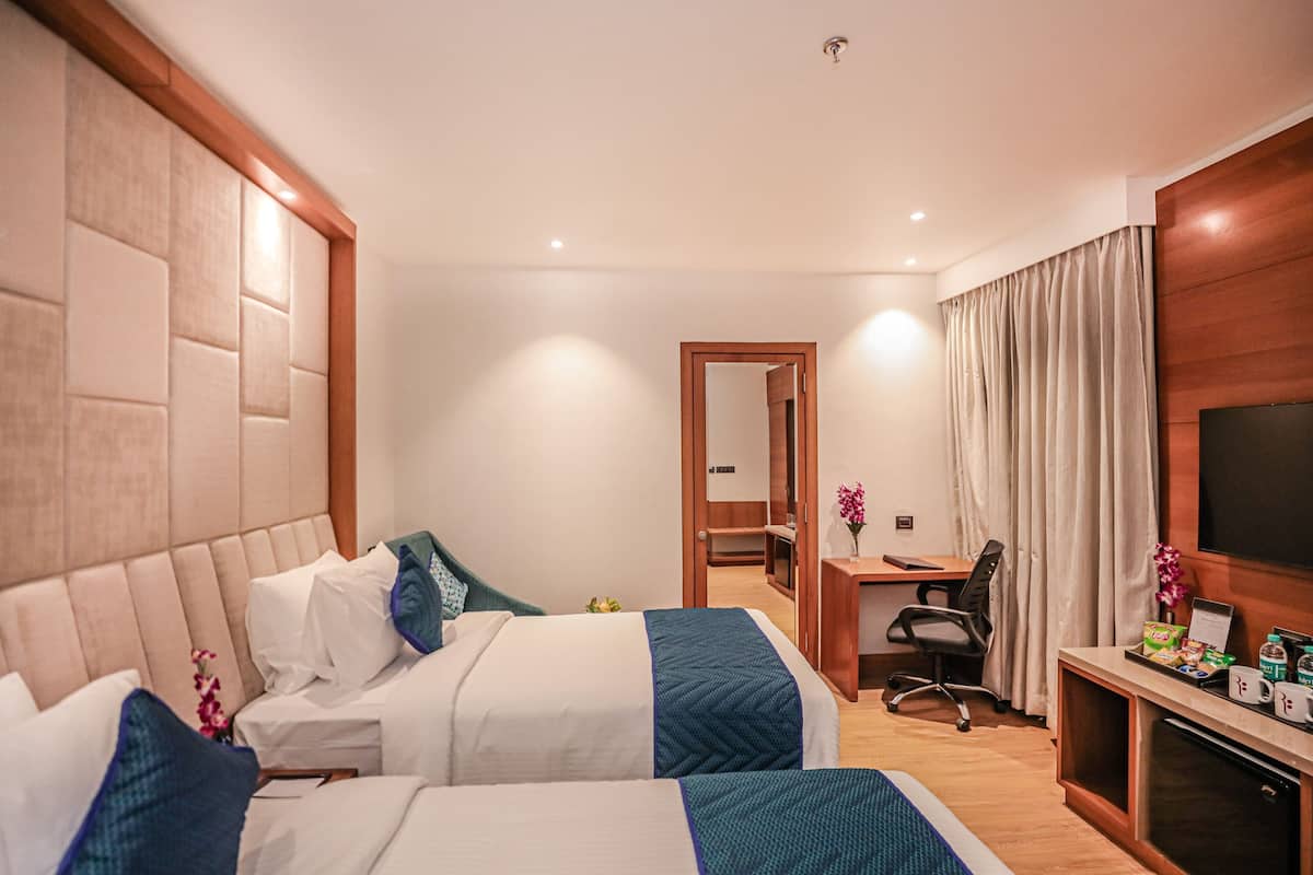 A hotel room with two beds, a desk, a TV, and a minibar.
