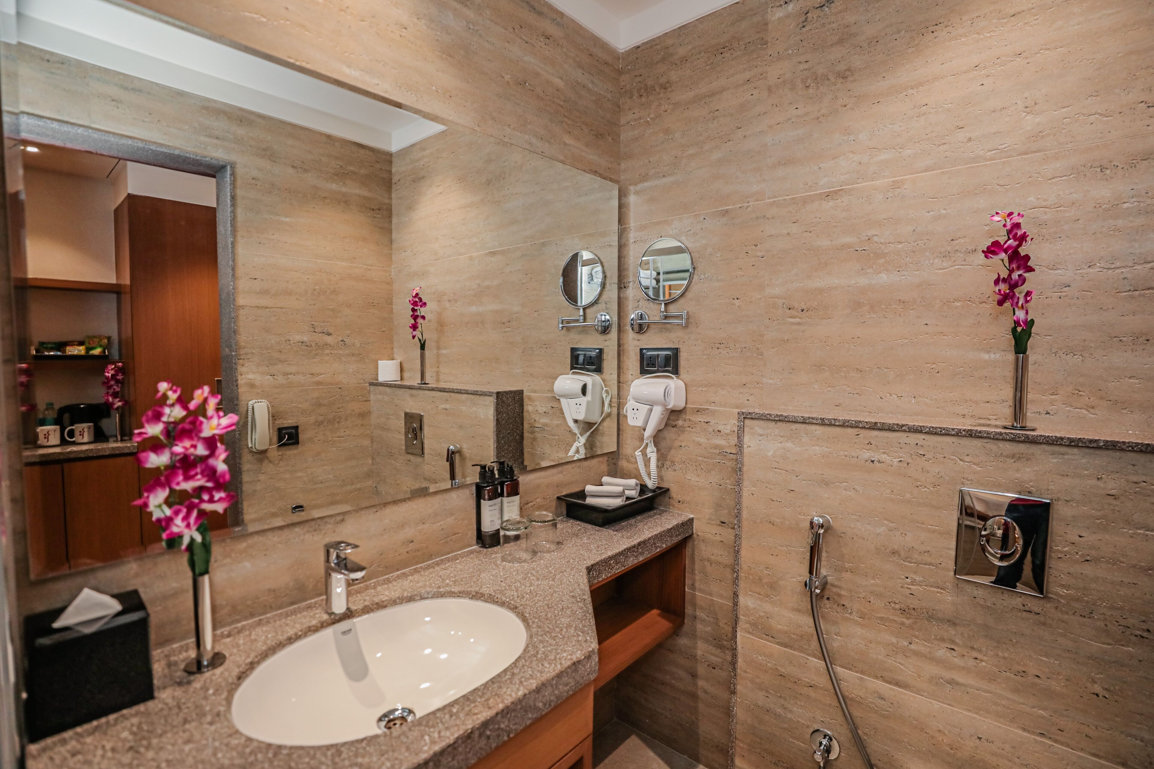 Un baño moderno con encimera de granito, un lavabo blanco, un espejo grande y un cabezal de ducha manual.